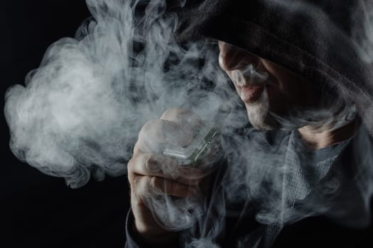 a man smokes a vape electronic cigarette in black clothes on a dark background, close-up, nicotine addiction, Harm of electronic cigarettes