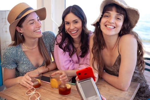 Three happy friends who are in the restaurant with drinks, pay with contactless payment via mobile phone app