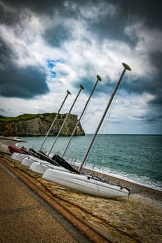 catamarans or boats with masts in a row on a beach in Normandy with the elephant rock of the chalk cliffs of Etretat in normandy