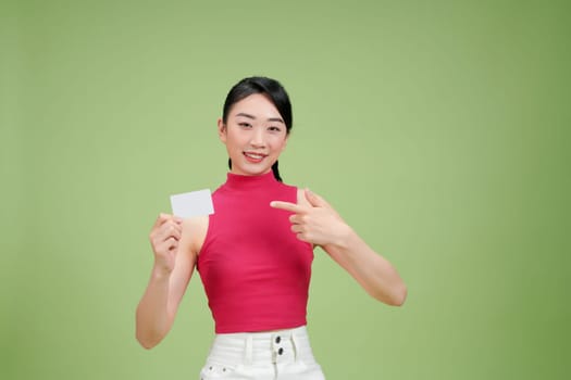 Smiling woman in red top and white pants holding and pointing at a blank card with a green background.