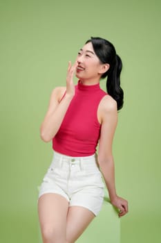 Smiling young woman sitting on a cube against a green backdrop. She looks happy and relaxed.