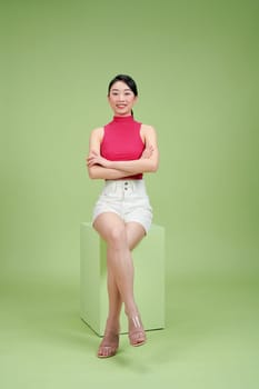 Confident woman sitting with crossed arms on a cube against a green background