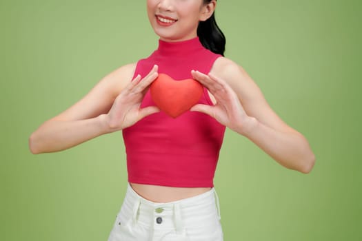 Young woman posing with a red heart in front of her face against a green background