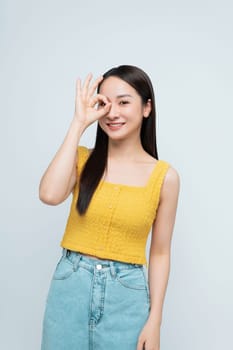 Young woman in a yellow top smiling and making an OK sign. Friendly expression and relaxed pose.