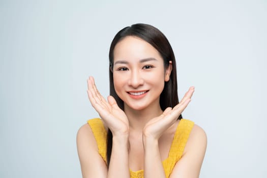 Cheerful young woman in a yellow top posing playfully with hands on face against a white background.