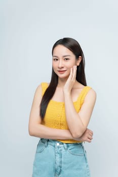 Portrait of a smiling woman wearing a yellow top and jeans, posing against a white background. She looks confident and happy.