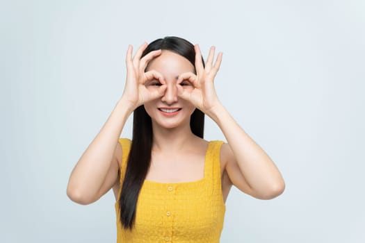 Smiling young woman in a yellow dress making a playful hand gesture with her fingers over her eyes, like glasses.