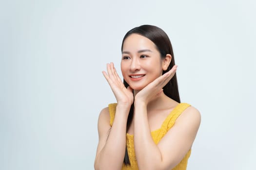 A cheerful young woman smiles while posing with her hands on her face, exuding happiness and joy.
