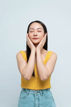 Happy young woman in a yellow top and jeans smiling joyfully with her hands near her face. 