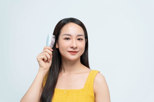 A young woman smiles confidently while holding a hairbrush against a light background, 