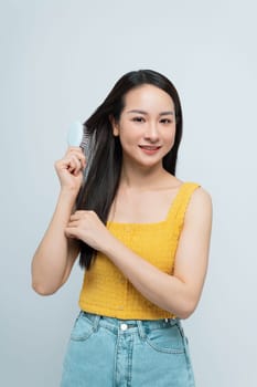 Young woman brushing her long dark hair while smiling, concept of personal grooming and hair care.