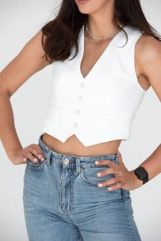 Happy beautiful girl posing in a new hot summer look. Wearing blue jeans and white waistcoat.