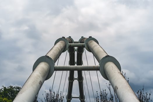 View from below of structural pipes forming part of a bridge, extending upwards against a cloudy sky. Showcases industrial design and strength.