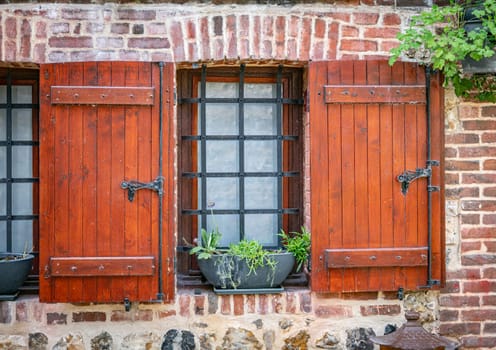 a window with wooden shutters and bars on the glass with a planter and an old stone wall