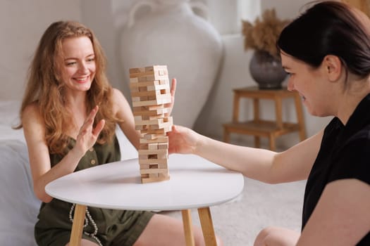 two women playing Jenga board game at home, excitement and relaxation, mind development concept, girl hands playing wooden game Django