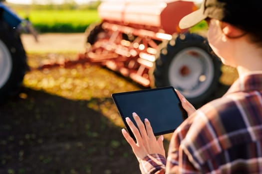 a girl agronomist with a tablet manages agribusiness against the background of a tractor, modern agribusiness