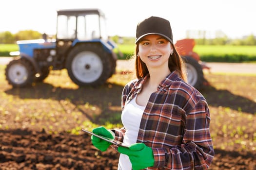 a girl agronomist with a tablet manages agribusiness against the background of a tractor, modern agribusiness
