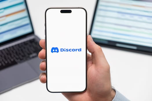 PRAGUE, CZECH REPUBLIC - JANUARY 21 2024: Discord logo on the screen of smartphone in mans hand on the workplace background.