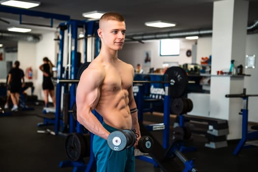A young blond man in a gym lifts weights with a focused expression