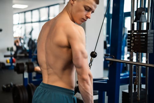 A young professional bodybuilder trains his triceps with a cable machine at the gym
