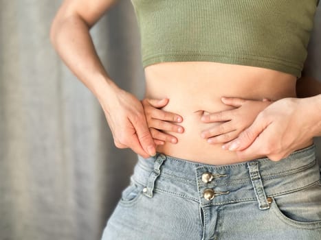 Close up of woman in jeans and green top with childs hands on her waist. Concept of family bonding, motherhood, and affection. Neutral background. High quality photo