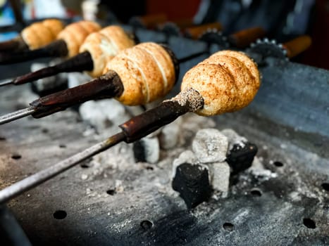 Trdelnik baking on metal rods over hot coals. Close up view of traditional Hungarian street food being prepared at market. Food and culinary concept for poster and print. High quality photo