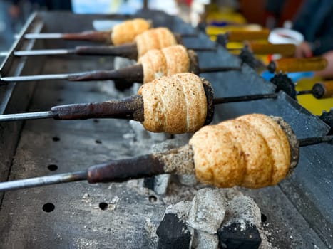 Trdelnik baking on metal rods over hot coals. Close up view of traditional Hungarian street food being prepared at market. Food and culinary concept for poster and print. High quality photo