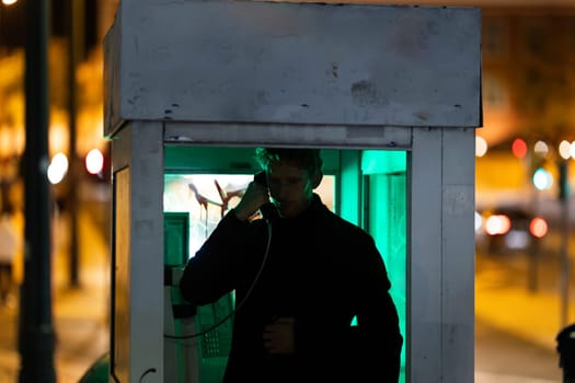 A man is talking on a phone at noir style in booth The image has a dark and moody atmosphere, with the man's face illuminated by the phone's light