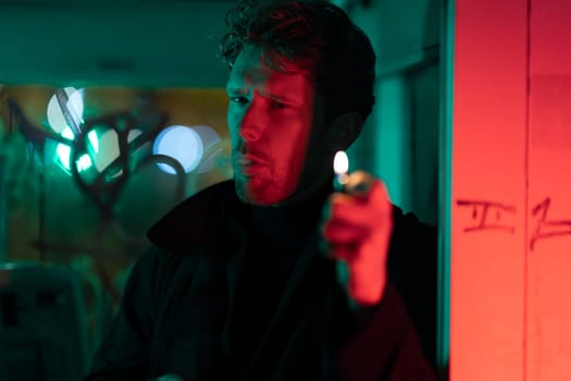 A man is smoking a cigarette in a telephone booth. The room is filled with a red and green glow, giving it a mysterious and eerie atmosphere. The man's face is obscured by the smoke