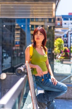 Vertical portrait of a cool asian woman standing relaxed in the city with skateboard