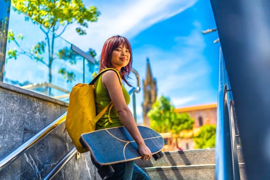 Cool asian young female skater turning to smile at camera walking up stairs in the city