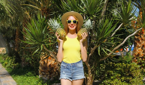 Summer vacation, tourism, happy smiling young woman with fruits, pineapple, joyful girl in glasses, straw tourist hat posing on the beach with palm tree