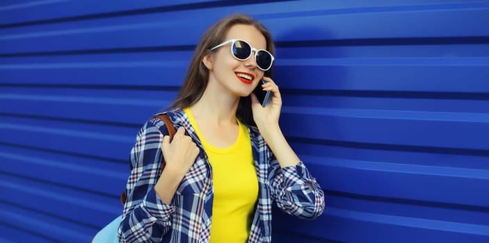 Happy young woman calling on phone, girl talking on the smartphone in glasses looks away on blue wall background