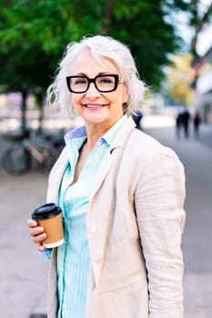 portrait of a stylish mature woman smiling happy looking at camera with a takeaway coffee in her hand, concept of active and urban lifestyle in adulthood