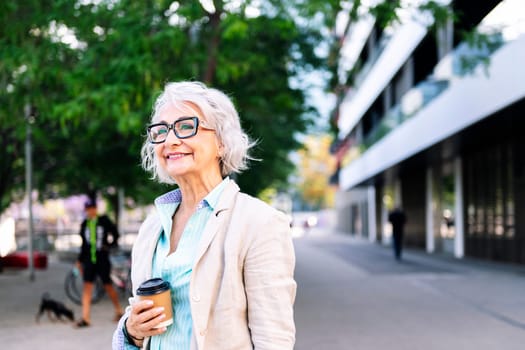 portrait of a stylish mature woman smiling happy at city with a takeaway coffee in her hand, concept of active and urban lifestyle in adulthood, copyspace for text