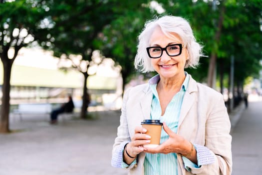 portrait of a beautiful mature woman smiling happy looking at camera with a takeaway coffee in her hand, concept of active and urban lifestyle in adulthood