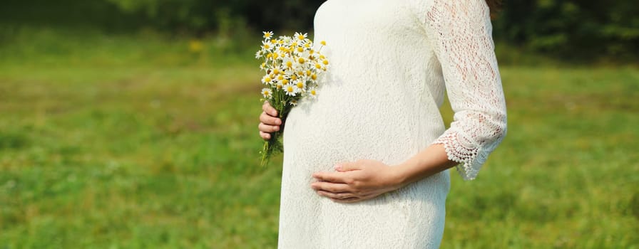 Pregnancy, maternity, happy young pregnant woman holding bouquet of flowers in dress standing in summer park
