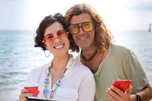 Middle aged man and woman standing on the beach with happy face, browsing smartphone apps. Concept:Vacation and Technology
