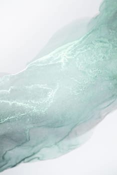 A close-up photograph of a light mint green ink swirl on a white background.