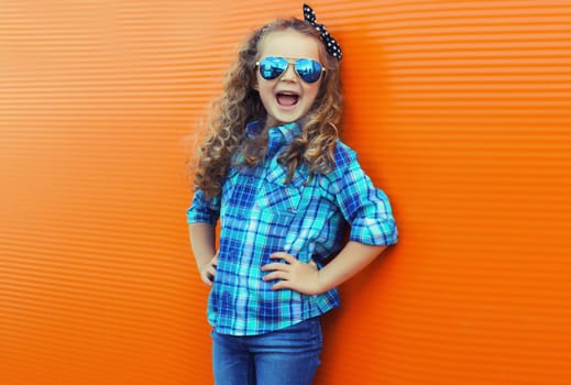 Happy cheerful kid girl with curly hair, joyful little child having fun on city street on orange wall background