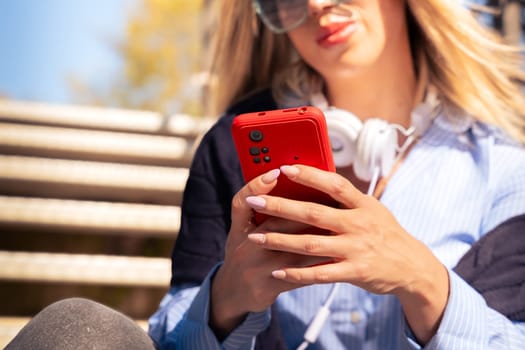 Portrait of a smiling young woman wearing headphones and sunglasses, using a social media app