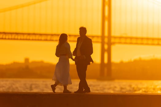A silhouette of a couple dancing in front of a bridge as the sun sets behind them.