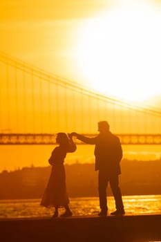 A silhouette of a man and woman dancing together at sunset. The bridge is visible in the background.