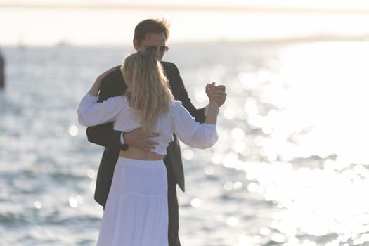 A man and woman dance together as the sun sets over the water.