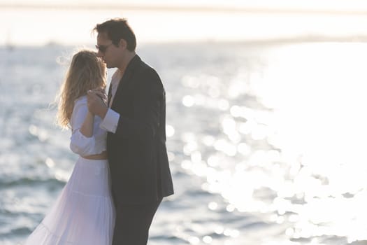 A couple dances on a beach as the sun sets, casting a golden glow over the water.