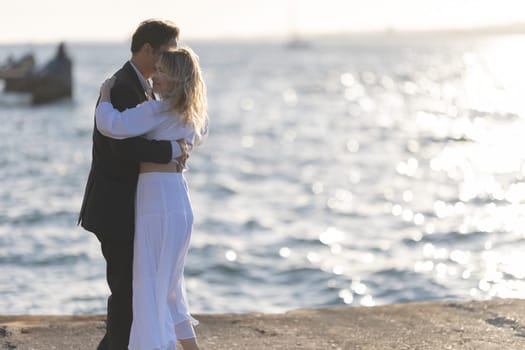 A man and woman dance on a rocky shoreline as the sun sets over the ocean.