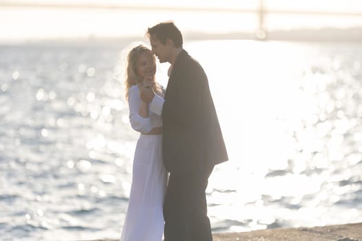 A man and woman dance together by a body of water, with the setting sun casting a warm glow.