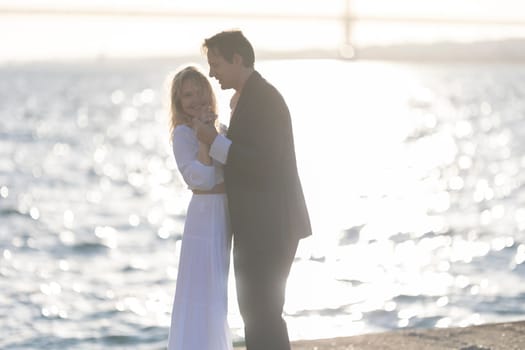 A man and woman dance together on a beach at sunset, with the water reflecting the golden light.