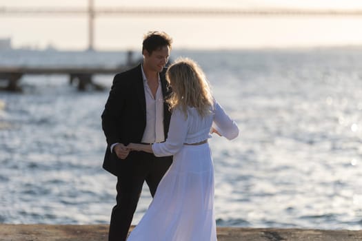 A woman and a man dance by the water's edge, enjoying the sunset together.