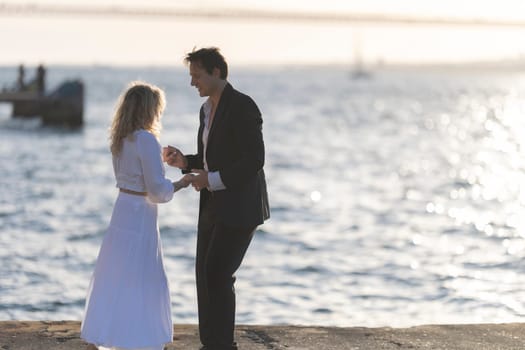 A man and woman dance together on a pier overlooking the ocean at sunset.